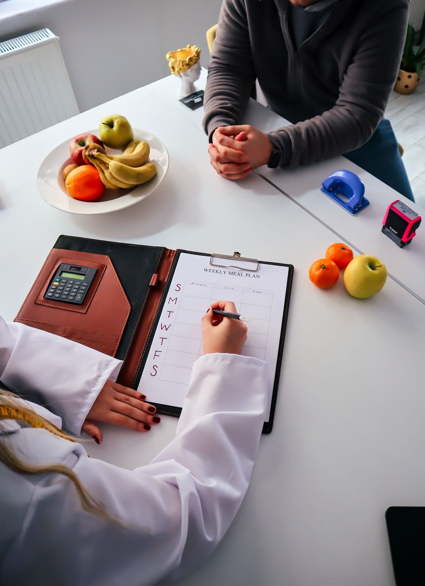 Nutricionista escribiendo un plan de comidas semanal junto a frutas frescas