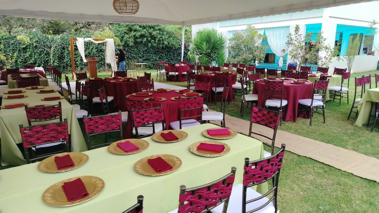 Evento en jardín con mesas montadas y sillas rojas